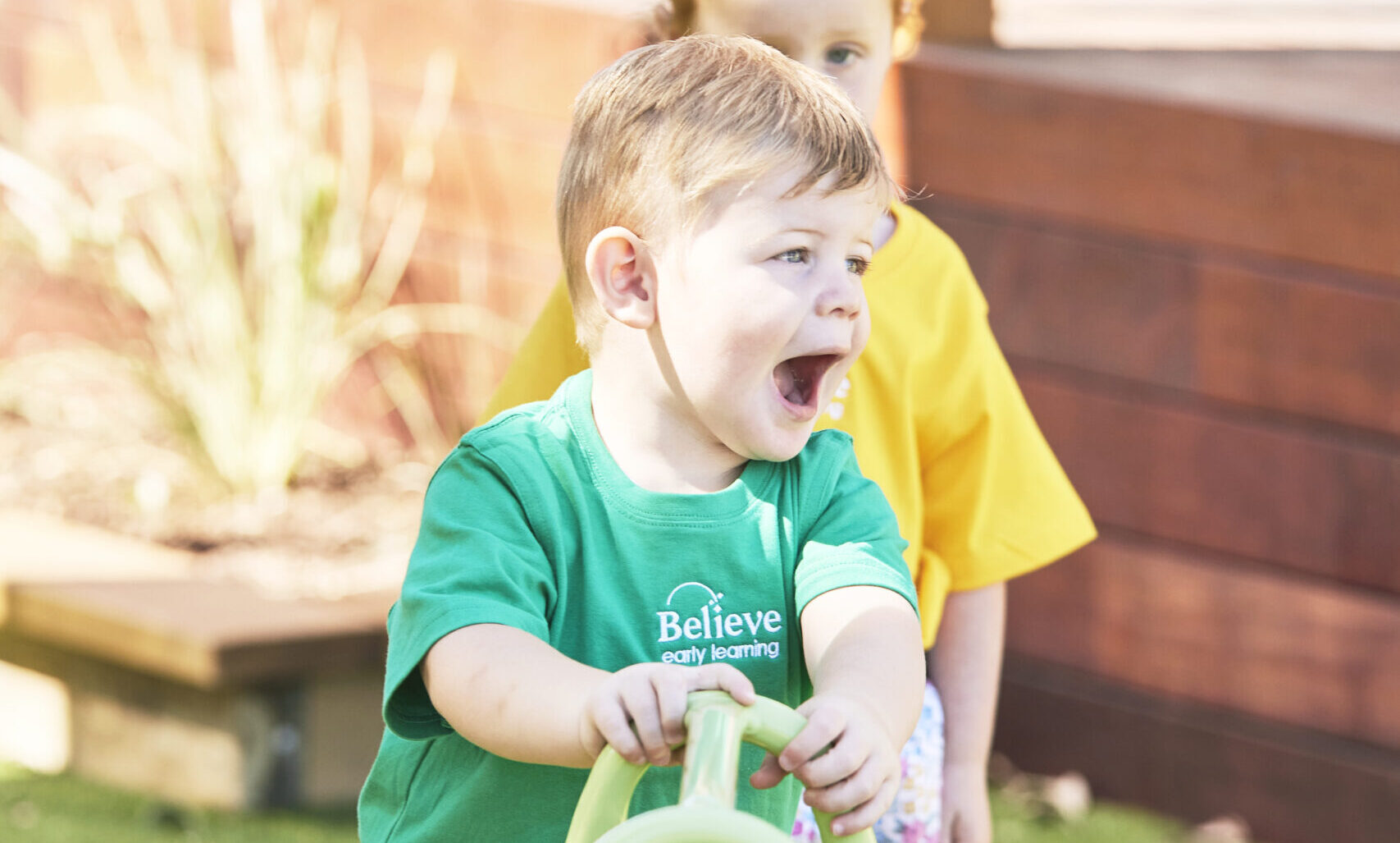 Happy toddler building confidence and gross motor skills outdoors with a toy in the playscape at Believe Early Learning Eaglehawk